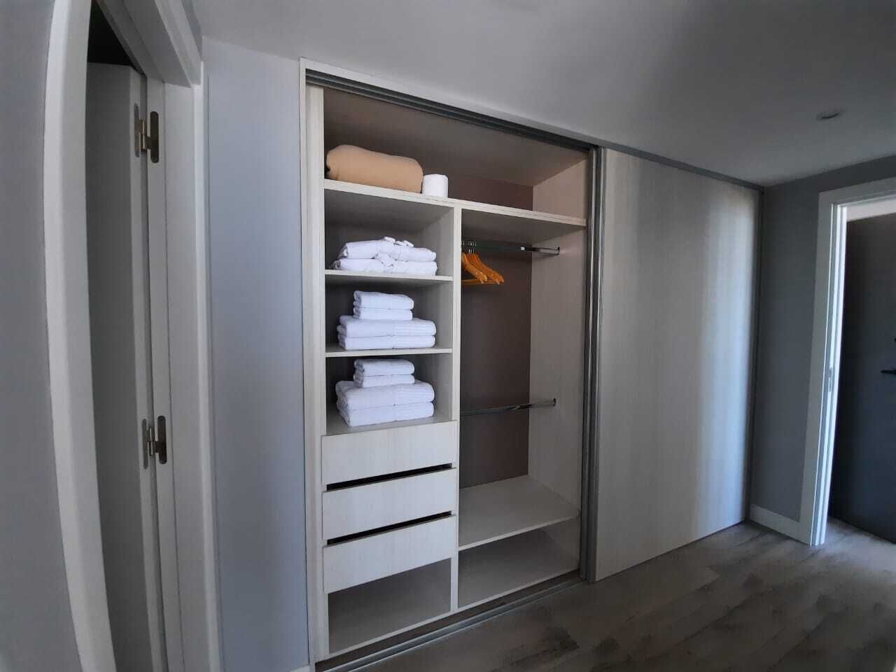 A walk-in closet with multiple shelves and hanging space, featuring neatly folded towels and a visible door handle.