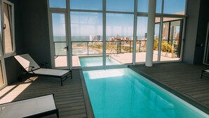 A modern indoor swimming pool with clear views of the ocean and cityscape through large windows. - Residencias Roque Suarez (Mar del Plata)