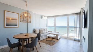 A modern living room with a dining area, large windows with a view of the sea, and a mounted TV. - Residencias Roque Suarez (Mar del Plata)
