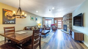 A spacious living area with a wooden dining table, leather sofas, a stone fireplace, and a mounted TV.