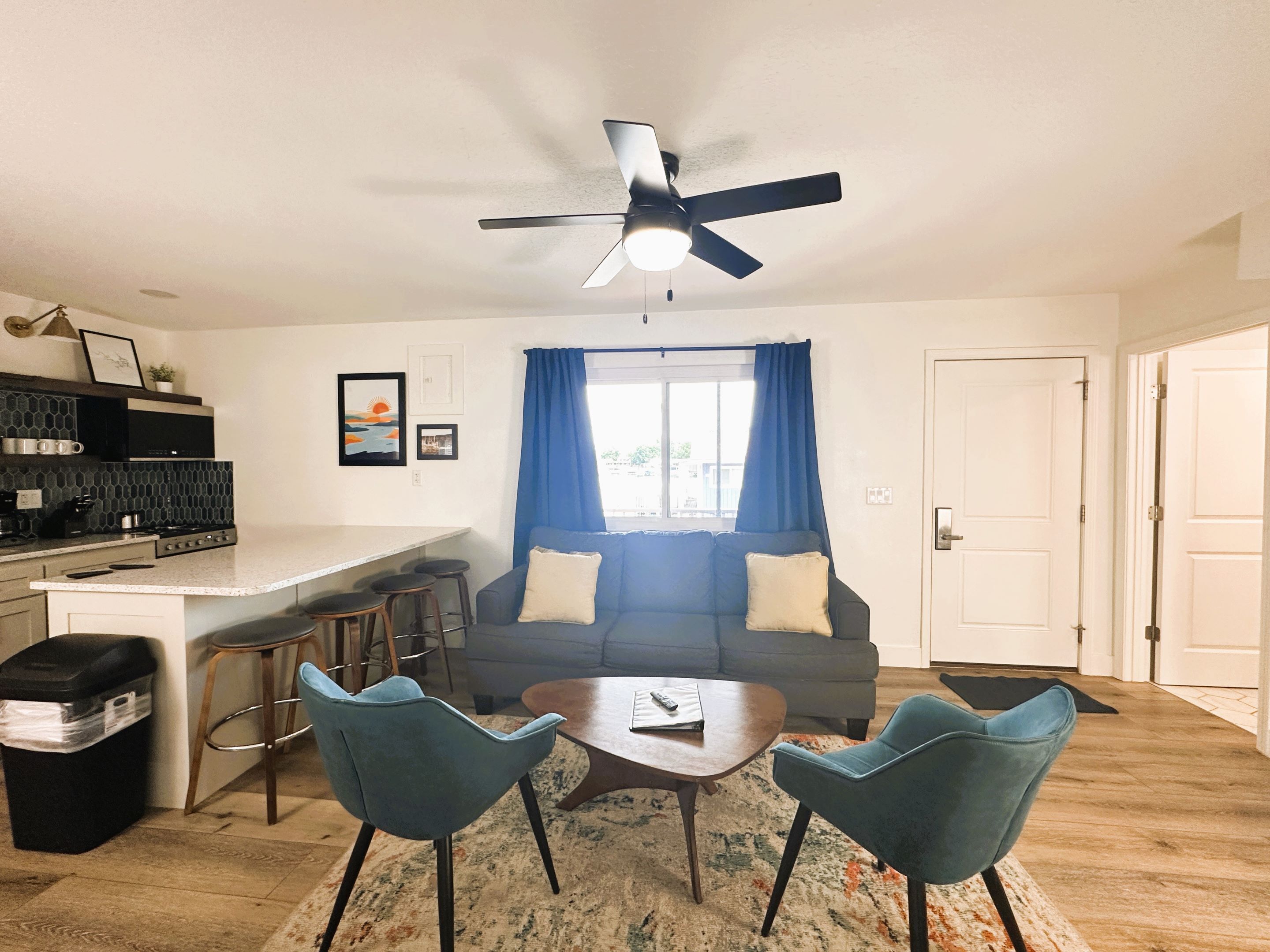 A compact living space with a kitchenette, a sofa, two chairs, a small table, and a ceiling fan.