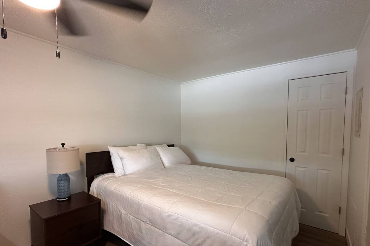 A bedroom with a bed, a nightstand, a lamp, and a door.