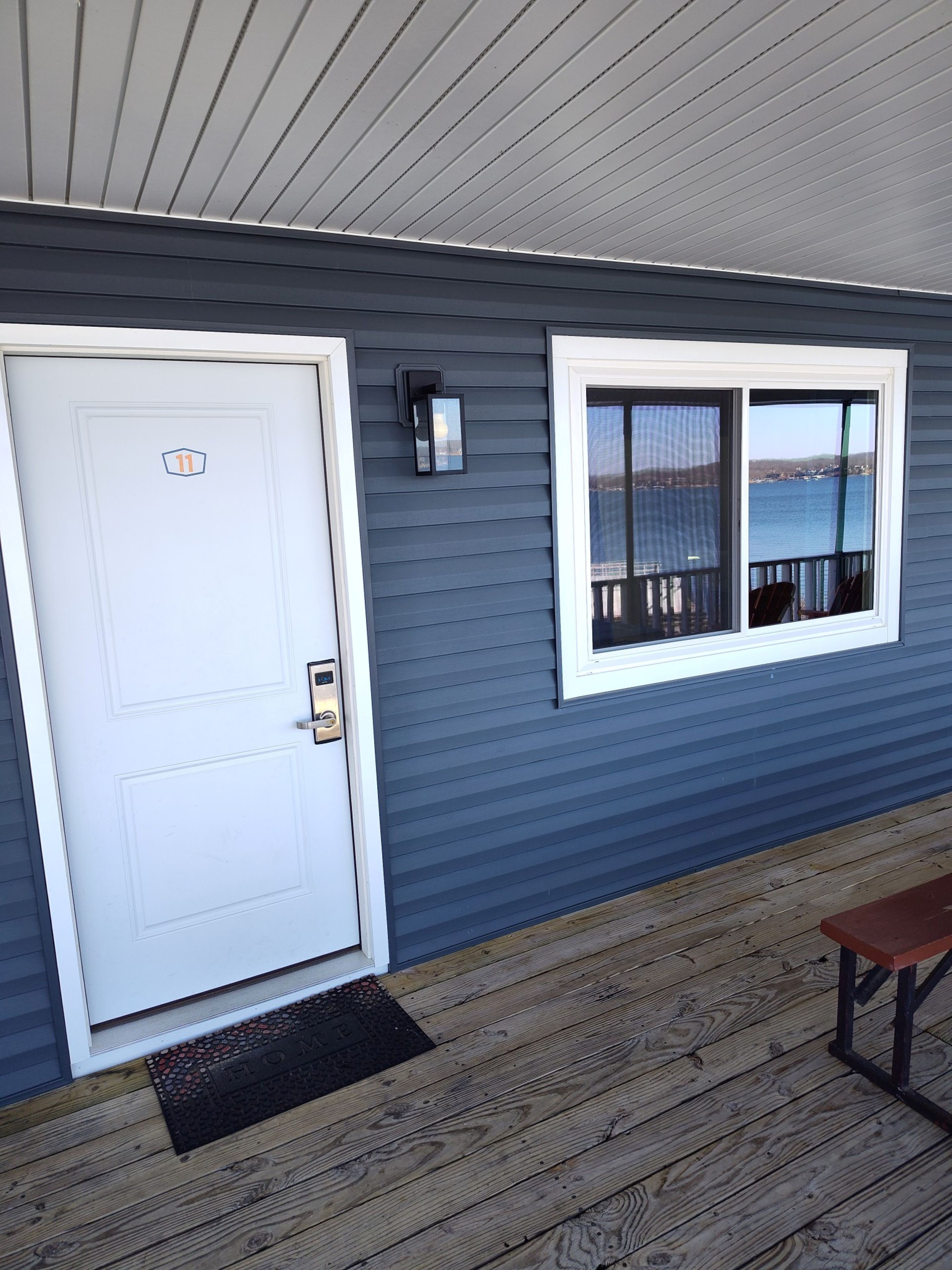 A house exterior with a white door, a window with a view of a body of water, and a wooden deck.