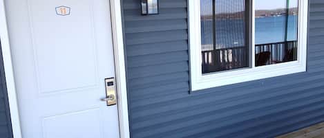 A house exterior with a white door, a window with a view of a body of water, and a wooden deck.