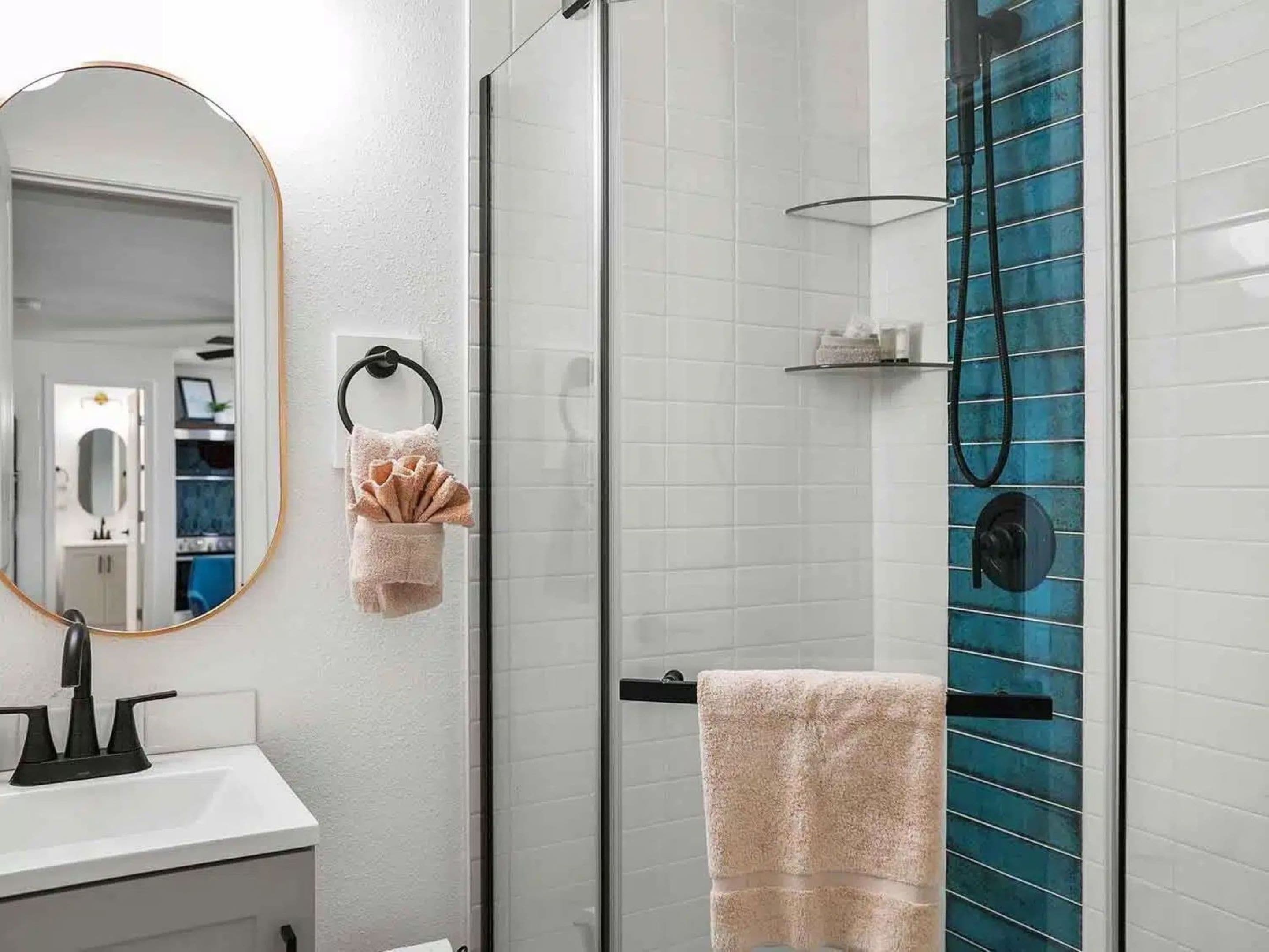 A modern bathroom with a glass shower enclosure, a white sink, a mirror, and a towel rack.