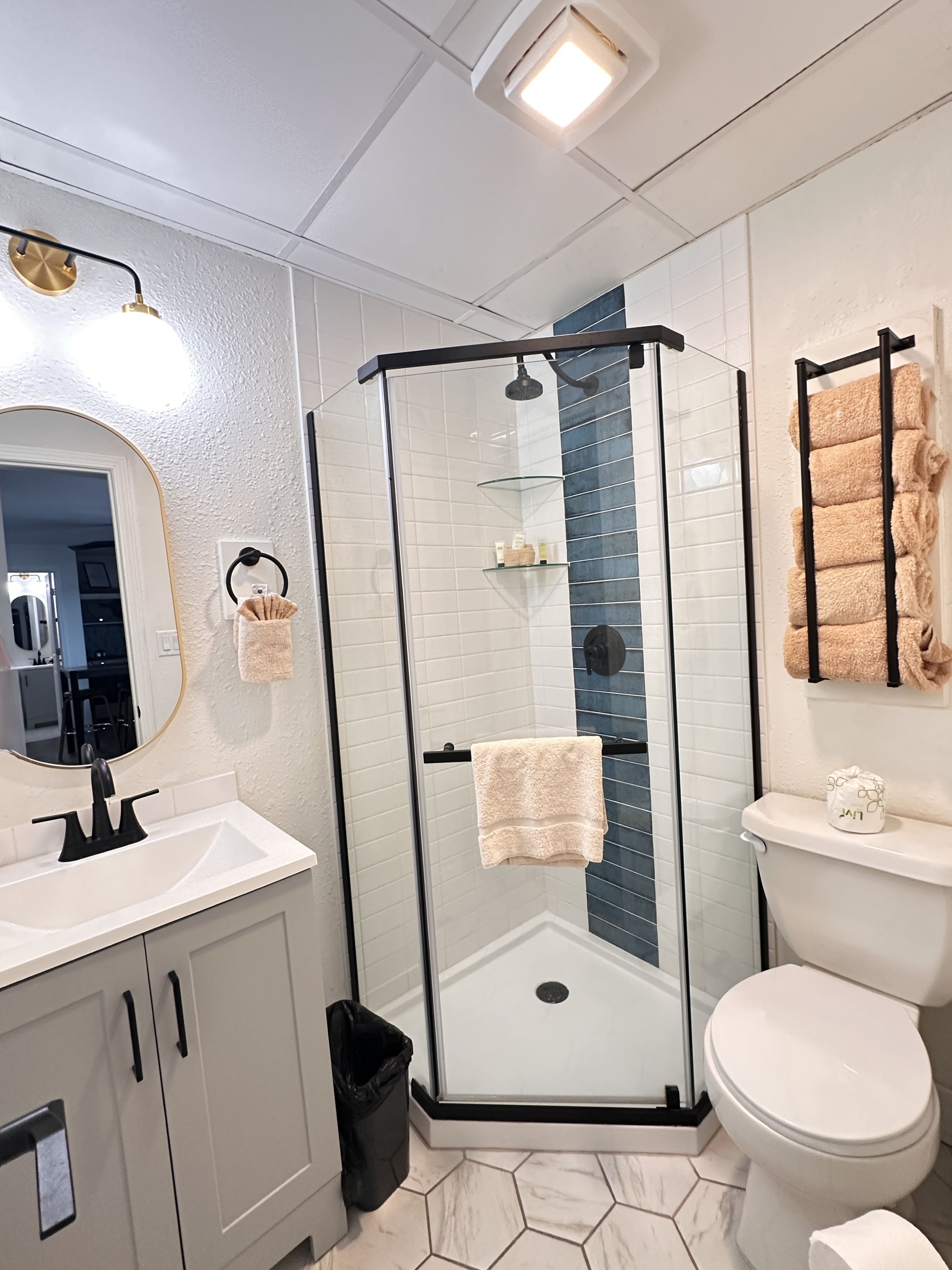 Ein modernes Badezimmer mit einer gläsernen Duschkabine, einem weißen Waschbecken, einer Toilette und einem Spiegel.