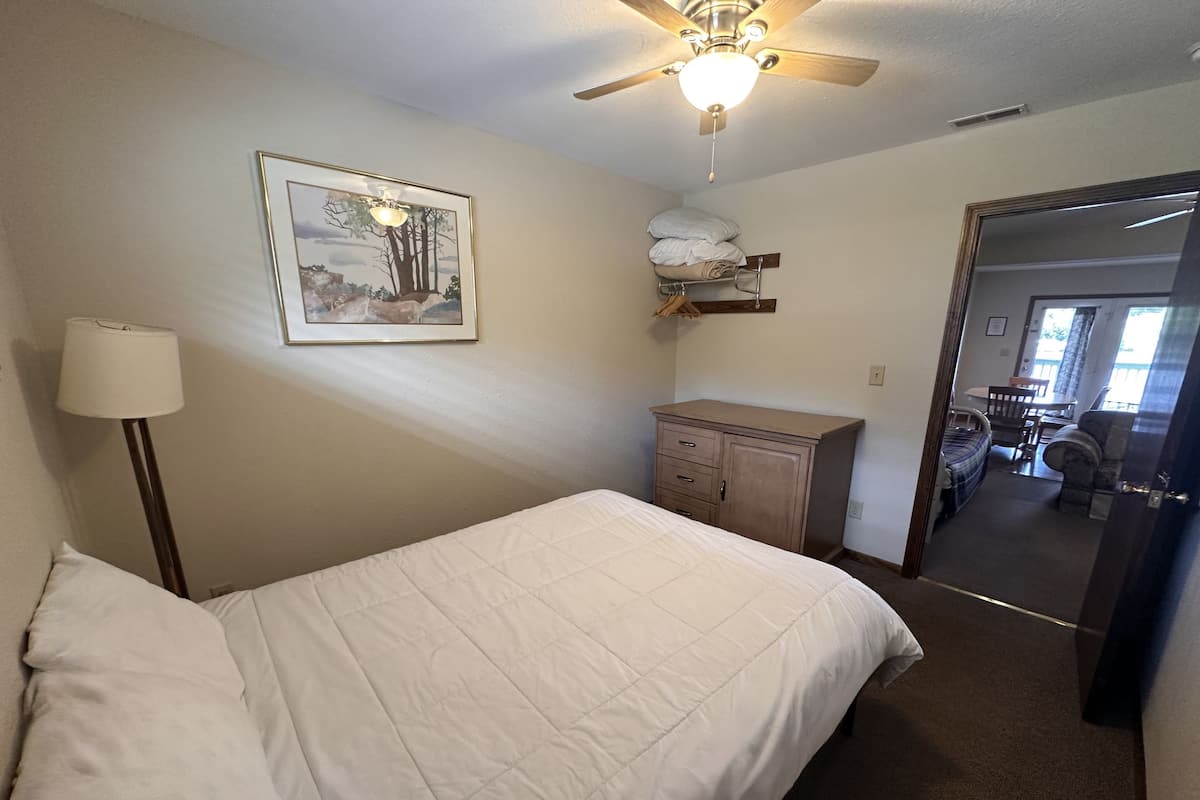 A bedroom with a bed, a dresser, a ceiling fan, and a framed picture on the wall.