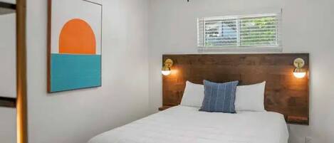 A bedroom with a bed, a ceiling fan, a window with blinds, and a wall-mounted artwork.