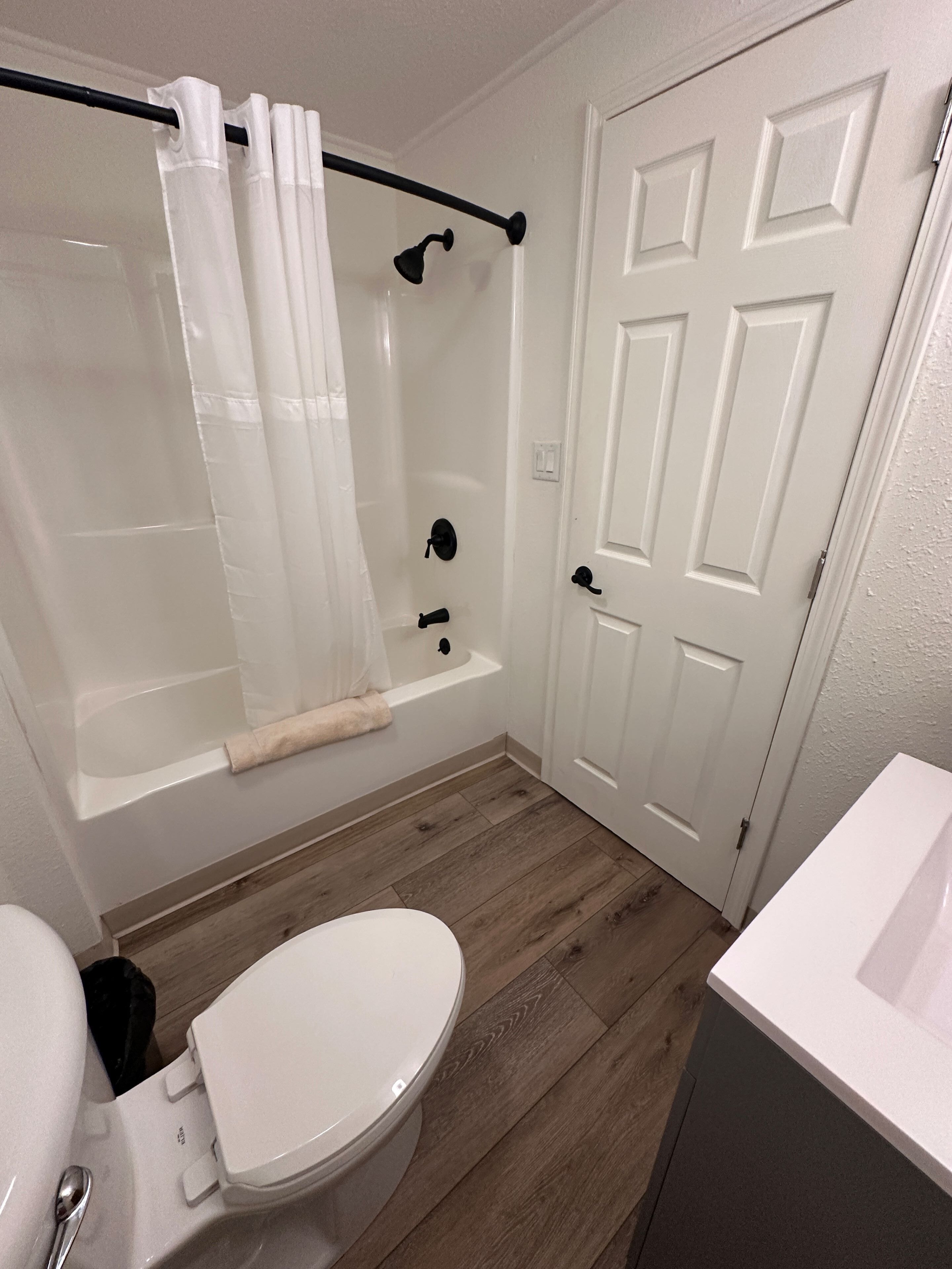Un bagno con un water bianco, una vasca da bagno con tenda doccia e una porta bianca.