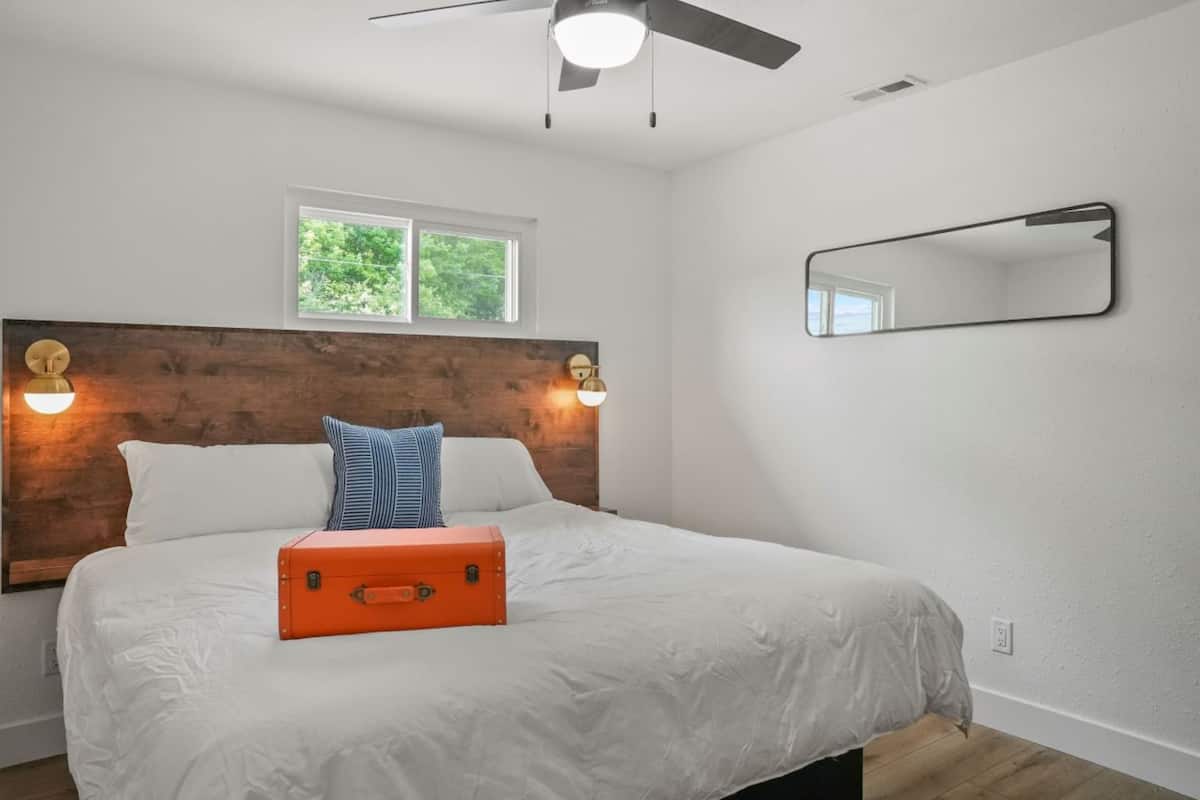 A bedroom with a wooden headboard, a window, a ceiling fan, and a bed with white bedding and an orange suitcase.