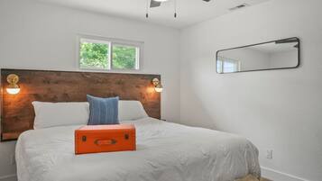 A bedroom with a wooden headboard, a window, a ceiling fan, and a bed with white bedding and an orange suitcase.