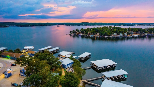 A marina with docked boats, a small dockside building, and a road with vehicles. - Alhonna Resort LLC (Lake Ozark)