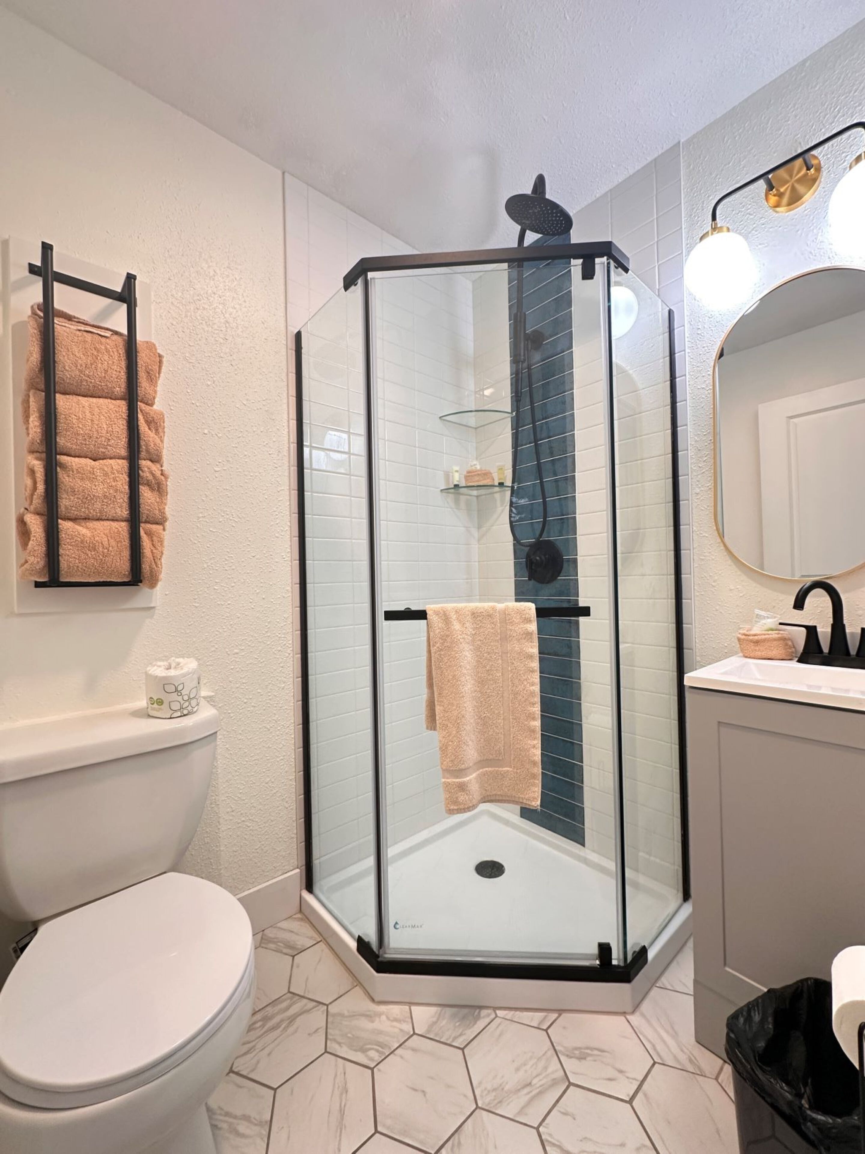 A modern bathroom with a glass-enclosed shower, a toilet, and a sink with a mirror.