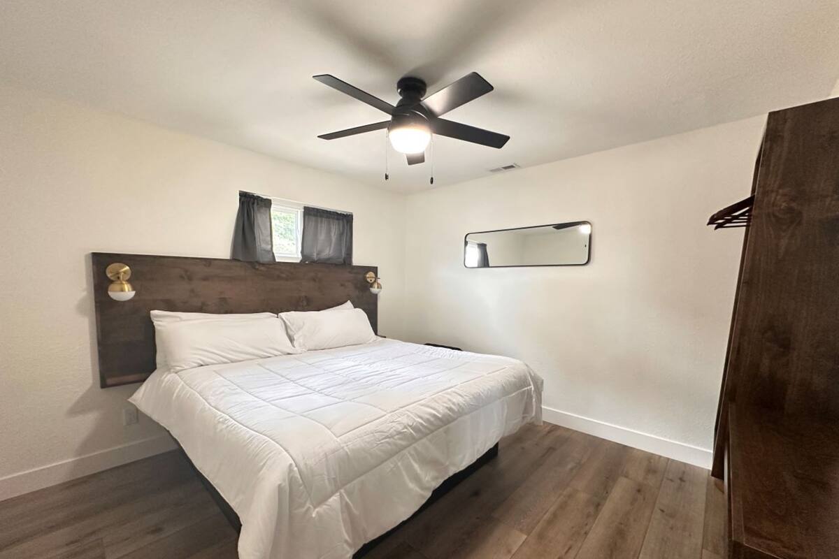 A bedroom with a bed, wooden floor, ceiling fan, and a mirror on the wall.