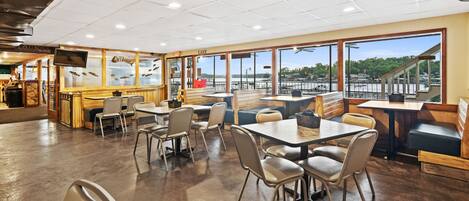 A spacious restaurant with high ceilings, large windows, and a view of the water.