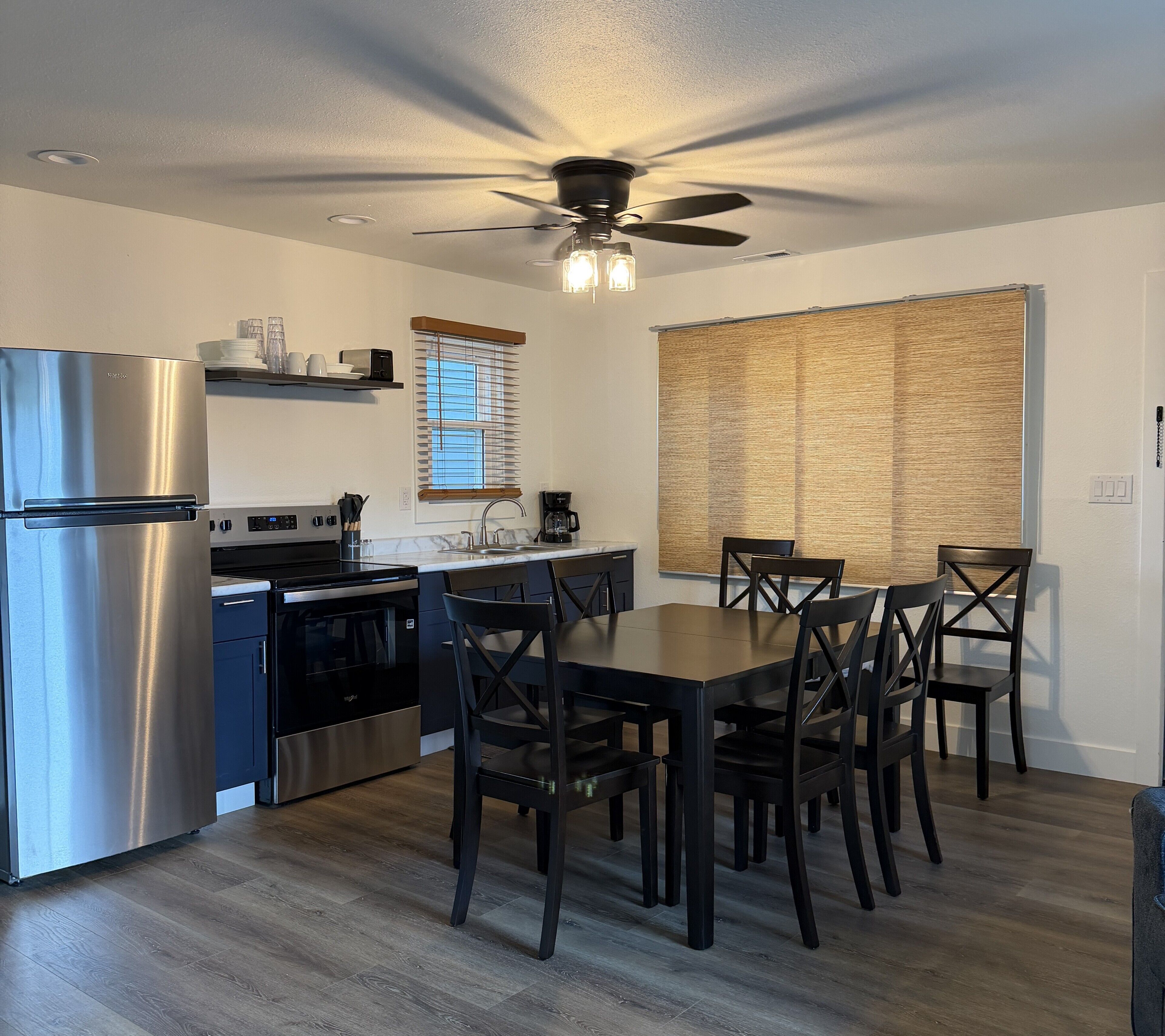 Cocina compacta con refrigerador, estufa, horno y mesa de comedor con sillas.