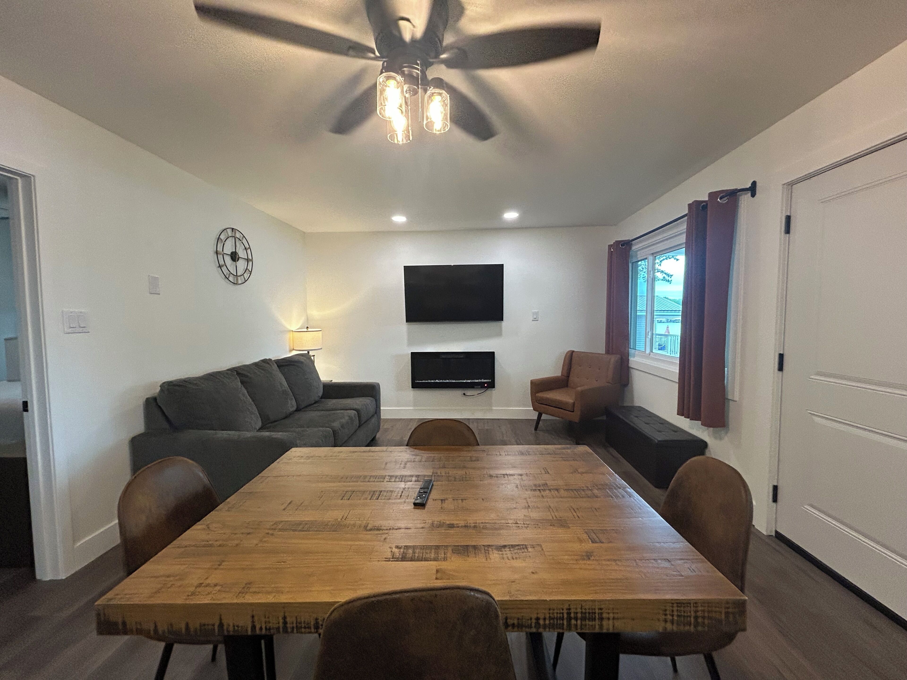 Una sala de estar con ventilador de techo, televisor de pantalla plana, sofá, sillón y mesa de comedor.