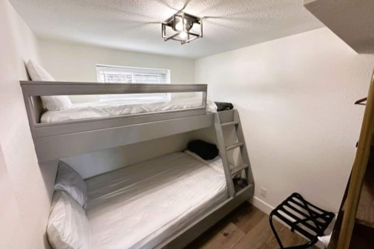 A bunk bed with a ladder, a small shelf, and a window with blinds.