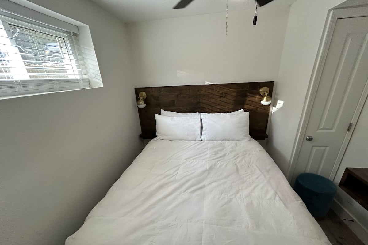 A single bed with white bedding, a wooden headboard, and two wall-mounted lamps.