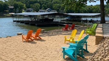 A lakeside beach with colorful Adirondack chairs and a dock extending into the water.
