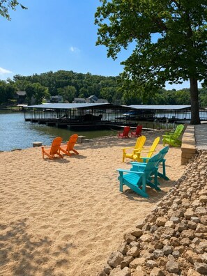 A lakeside beach with colorful Adirondack chairs and a dock extending into the water. - Alhonna Resort LLC (Lake Ozark)