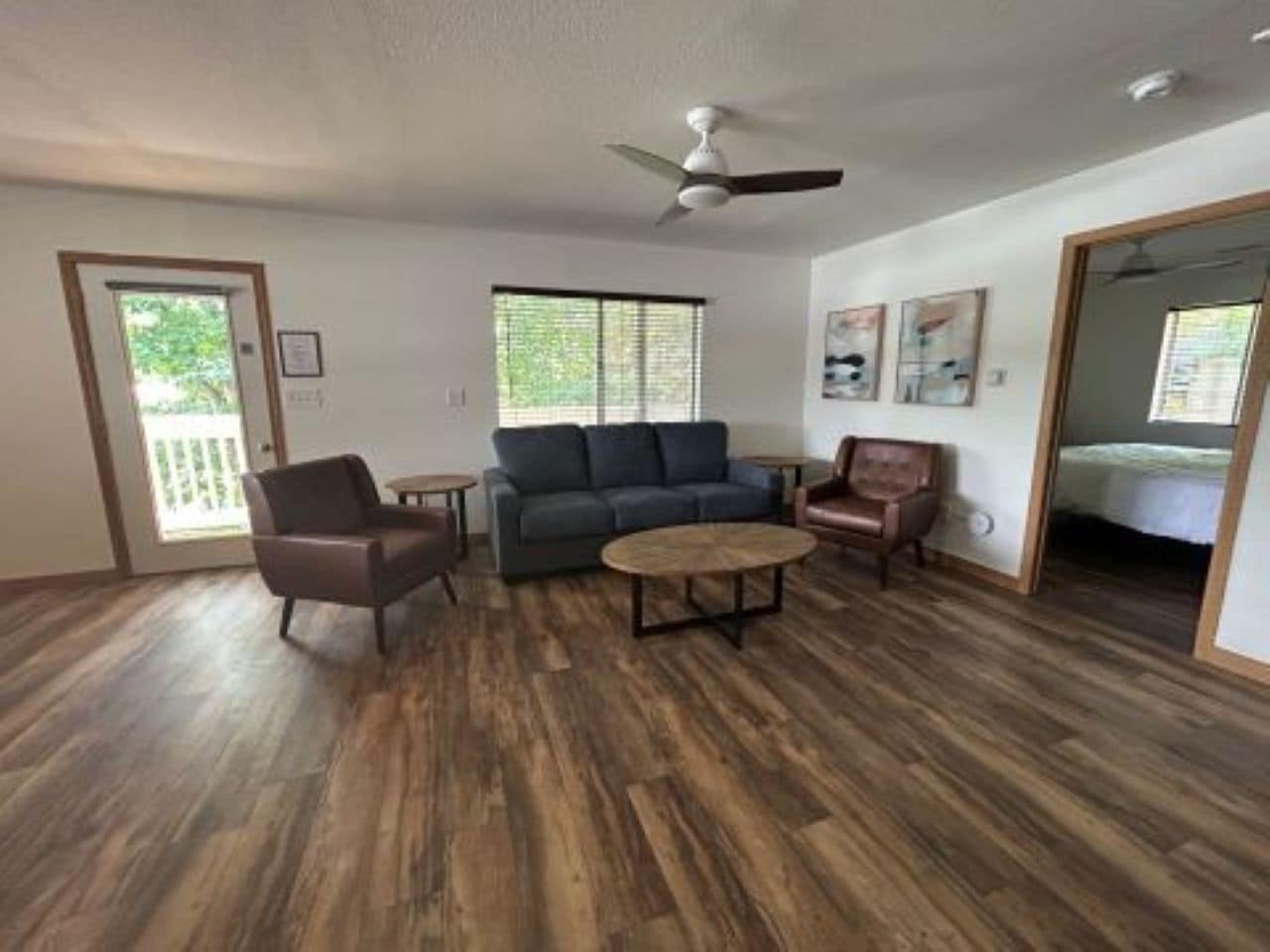 A spacious living room with a dark wood floor, a gray sofa, a brown leather chair, and a round coffee table.