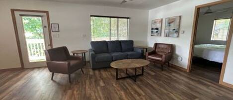 A spacious living room with a dark wood floor, a gray sofa, a brown leather chair, and a round coffee table.