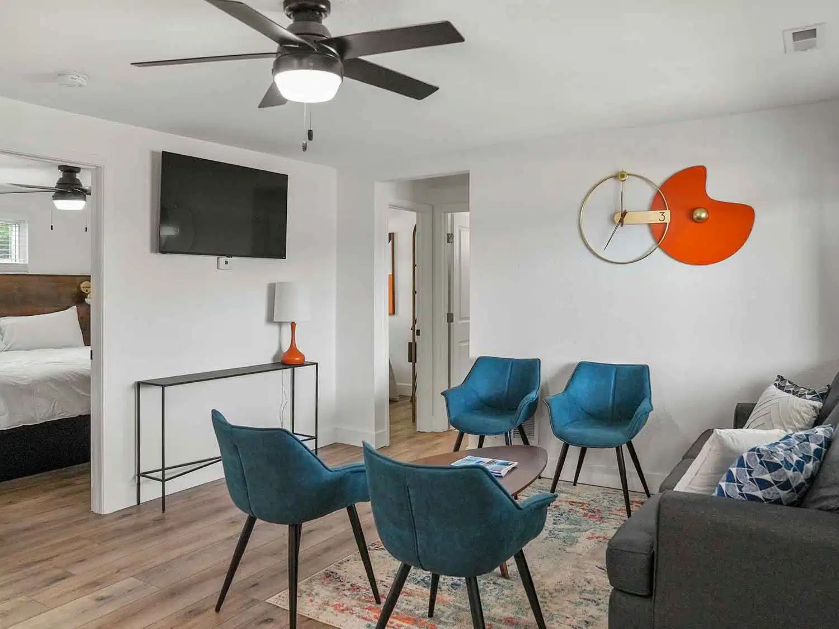 A modern living room with a ceiling fan, a TV, and a dining area with blue chairs and a table.