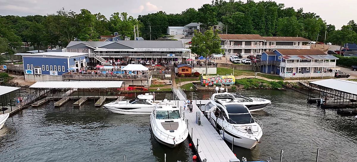 A marina with boats docked, a pier with people, and buildings in the background.