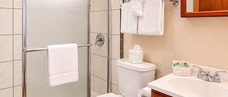 A bathroom with a glass shower enclosure, a toilet, a sink with a mirror, and a towel rack.
