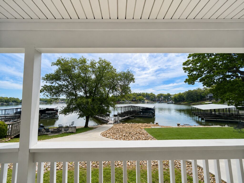 A lakeside view from a covered deck with a grassy area, dock, and trees.