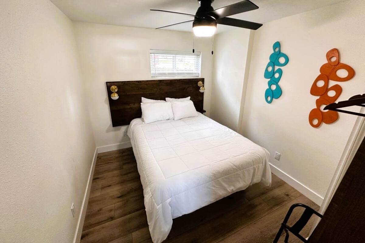 A bedroom with a bed, wooden flooring, a ceiling fan, and a window.