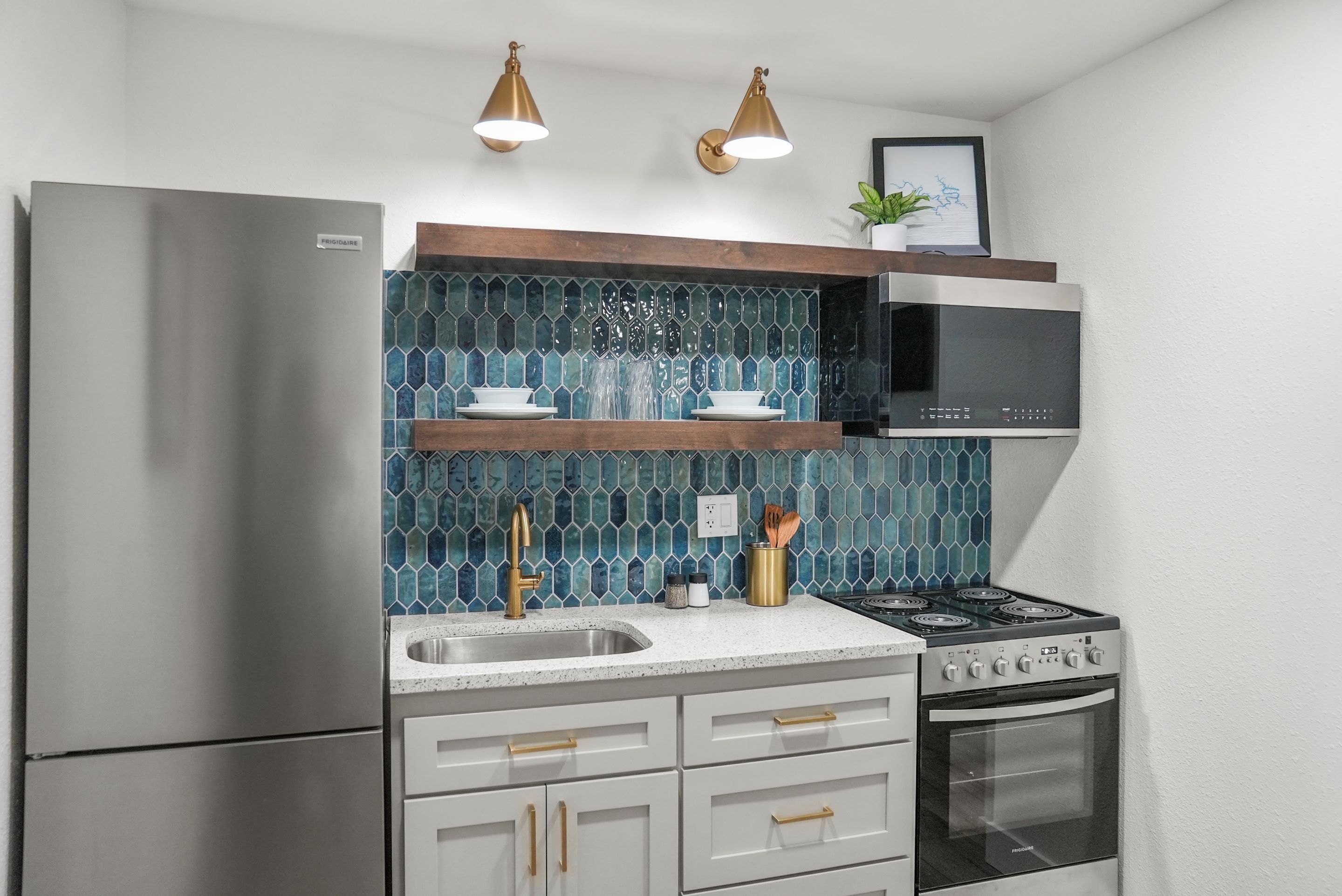 Una cocina moderna con electrodomésticos de acero inoxidable, un salpicadero de azulejos azules e accesorios dorados.