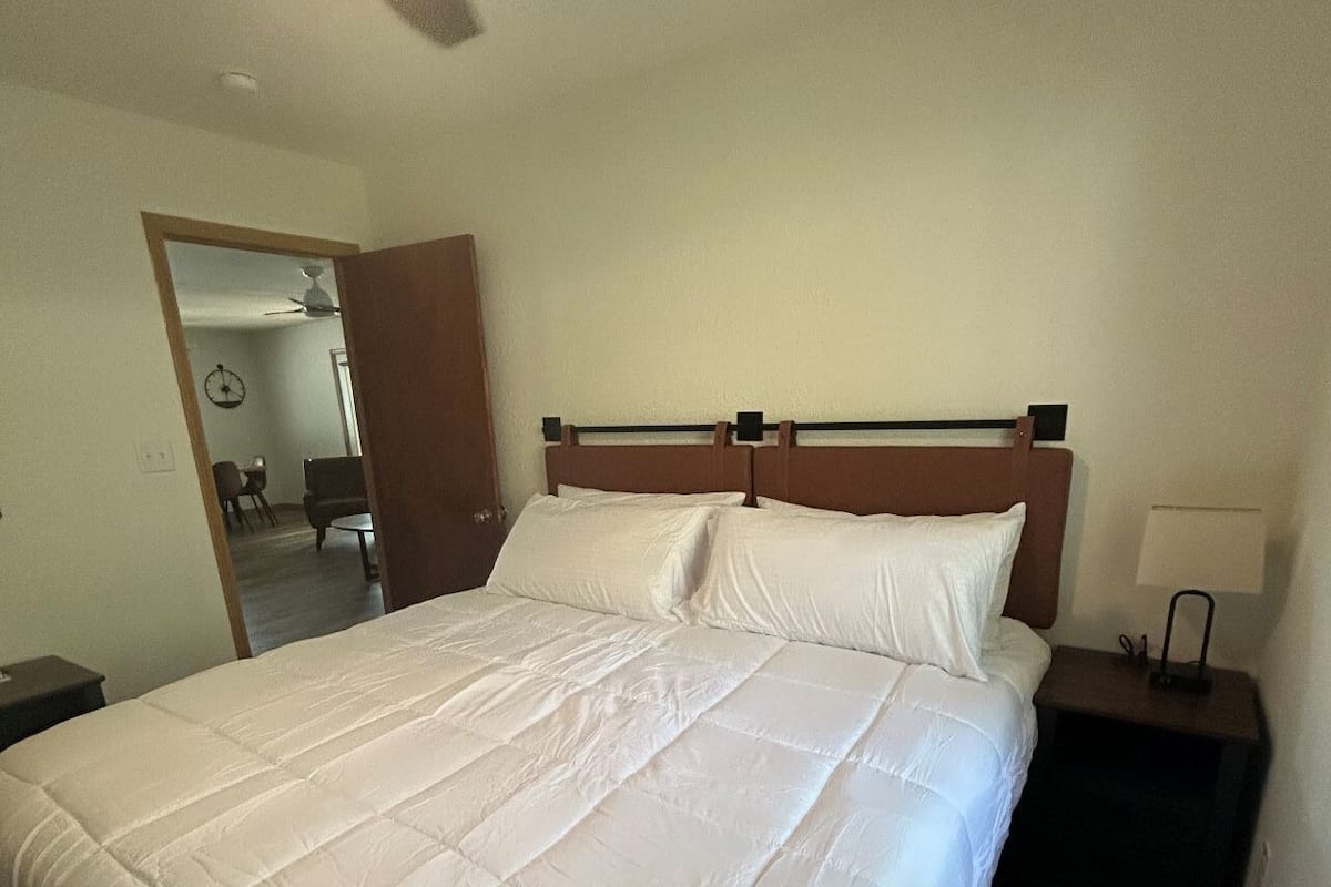 A neatly made bed with a wooden headboard, a bedside table with a lamp, and a ceiling fan.