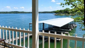 A waterfront view from a covered deck with a white railing, docked boats, and a distant shoreline. - Alhonna Resort LLC (Lake Ozark)