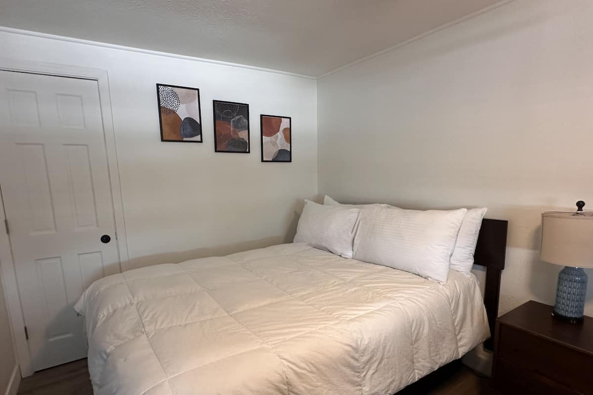 A bedroom with a bed, a nightstand, a lamp, and three framed artworks on the wall.