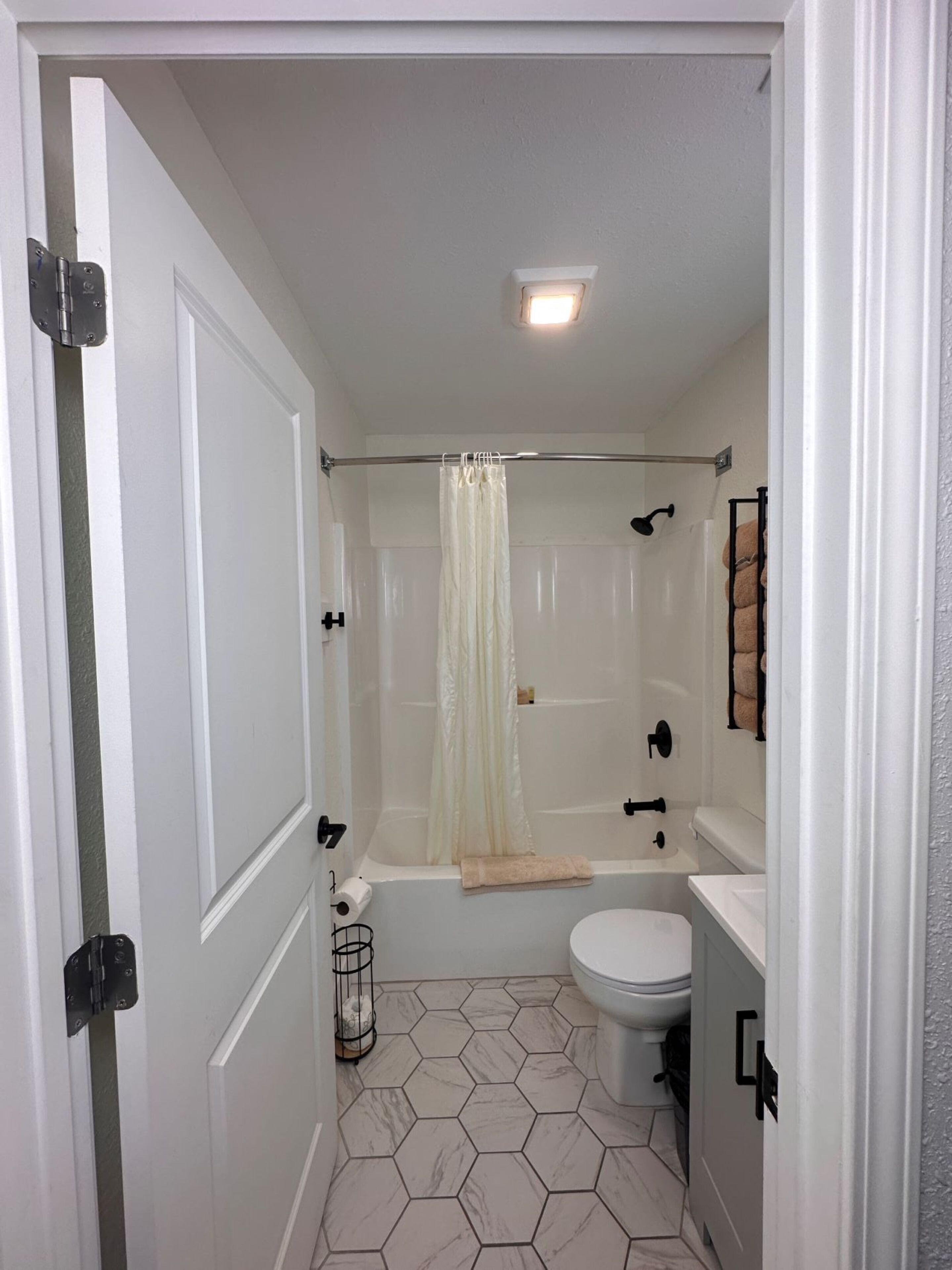 A bathroom with a shower, toilet, and sink, featuring hexagonal tile flooring and a white color scheme.