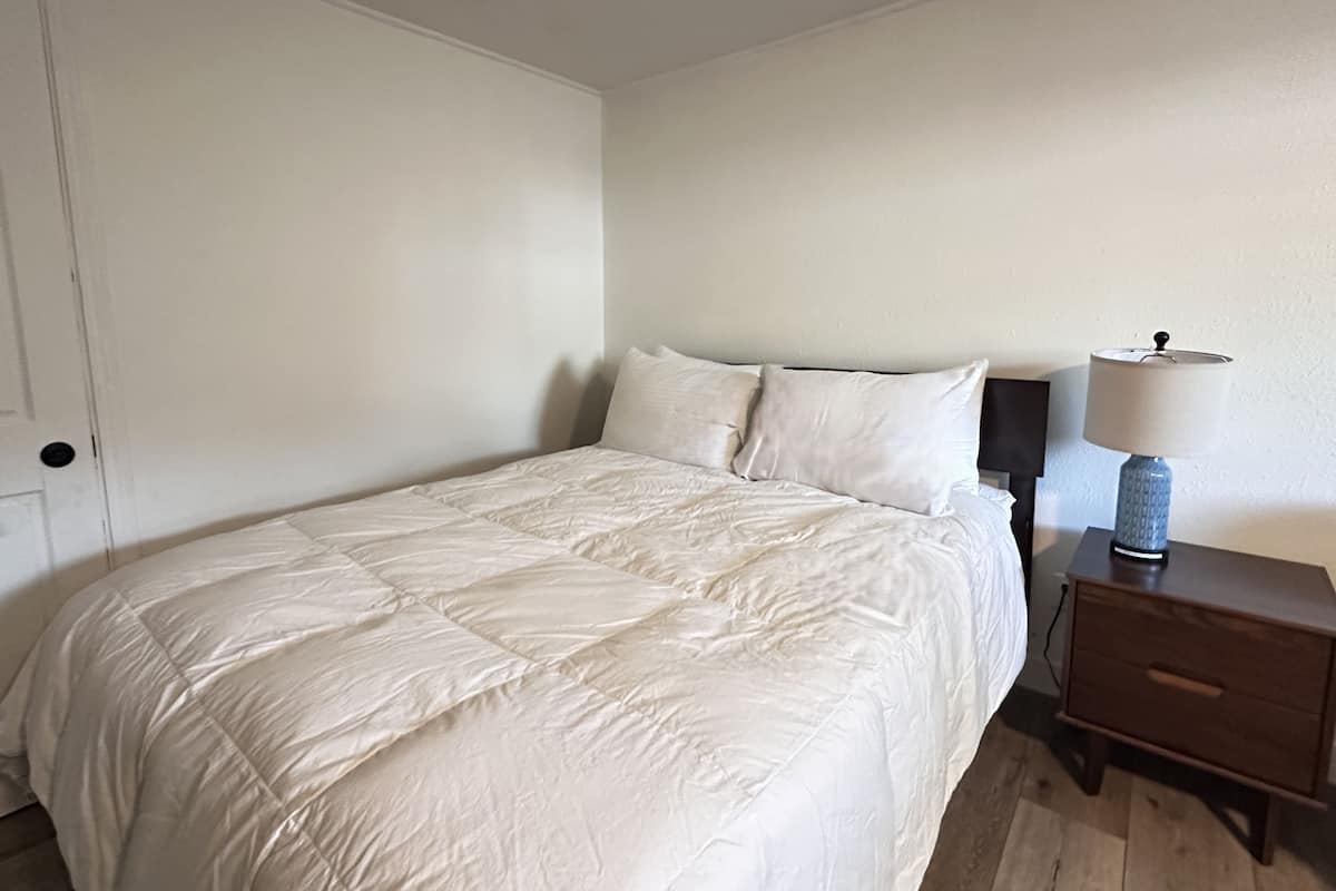 A neatly made bed with a white duvet, a bedside table with a lamp, and a wooden nightstand.