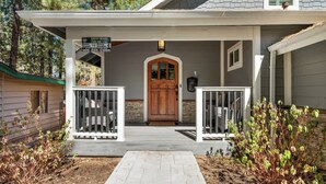 A house with a front porch, a wooden door, and a signboard. - Pine Summit | Hot Tub+Sauna | BBQ | Arcade + Games (Big Bear Lake)