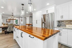 Una cocina moderna con armarios blancos, una isla de madera, electrodomésticos de acero inoxidable e iluminación colgante.