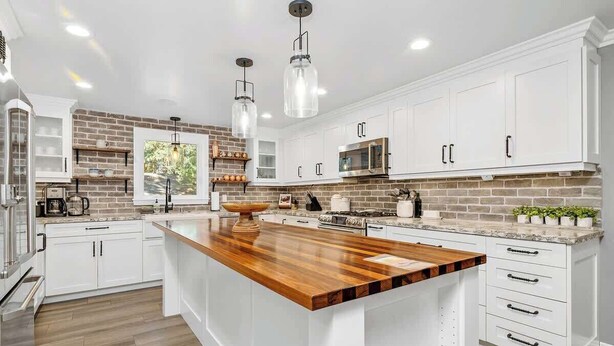 A modern kitchen with white cabinetry, a central island, and hanging pendant lights. - Pine Summit | Hot Tub+Sauna | BBQ | Arcade + Games (Big Bear Lake)