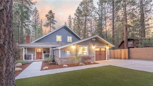 A two-story house with a stone foundation, a front porch, and a well-maintained lawn. - Pine Summit | Hot Tub+Sauna | BBQ | Arcade + Games (Big Bear Lake)