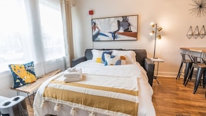 A hotel room with a bed, a desk, a chair, a lamp, and a painting on the wall. - Chic Getaway Downtown Hub Luxe Linens Near Transit (Redding)