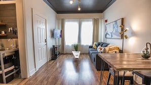 A modern living room with a sofa, a coffee table, a TV, and a dining area with a table and chairs. - Chic Getaway Downtown Hub Luxe Linens Near Transit (Redding)