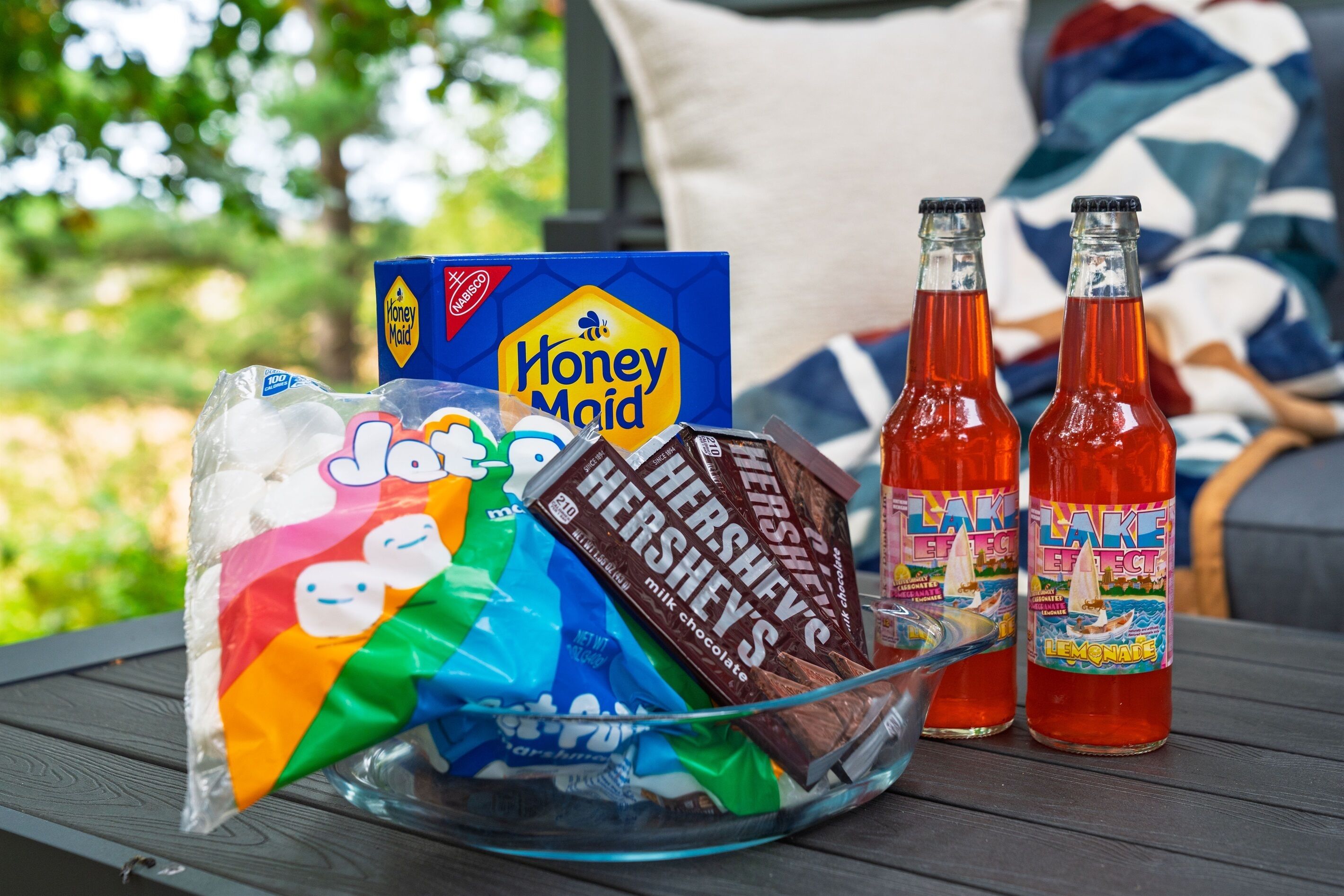 Un pique-nique est installé sur une table en bois : on y trouve un sac de bonbons Jolly Rancher, une boîte de biscuits Honey Maid, deux bouteilles de limonade Lake Effect et deux tablettes de chocolat Hershey's.