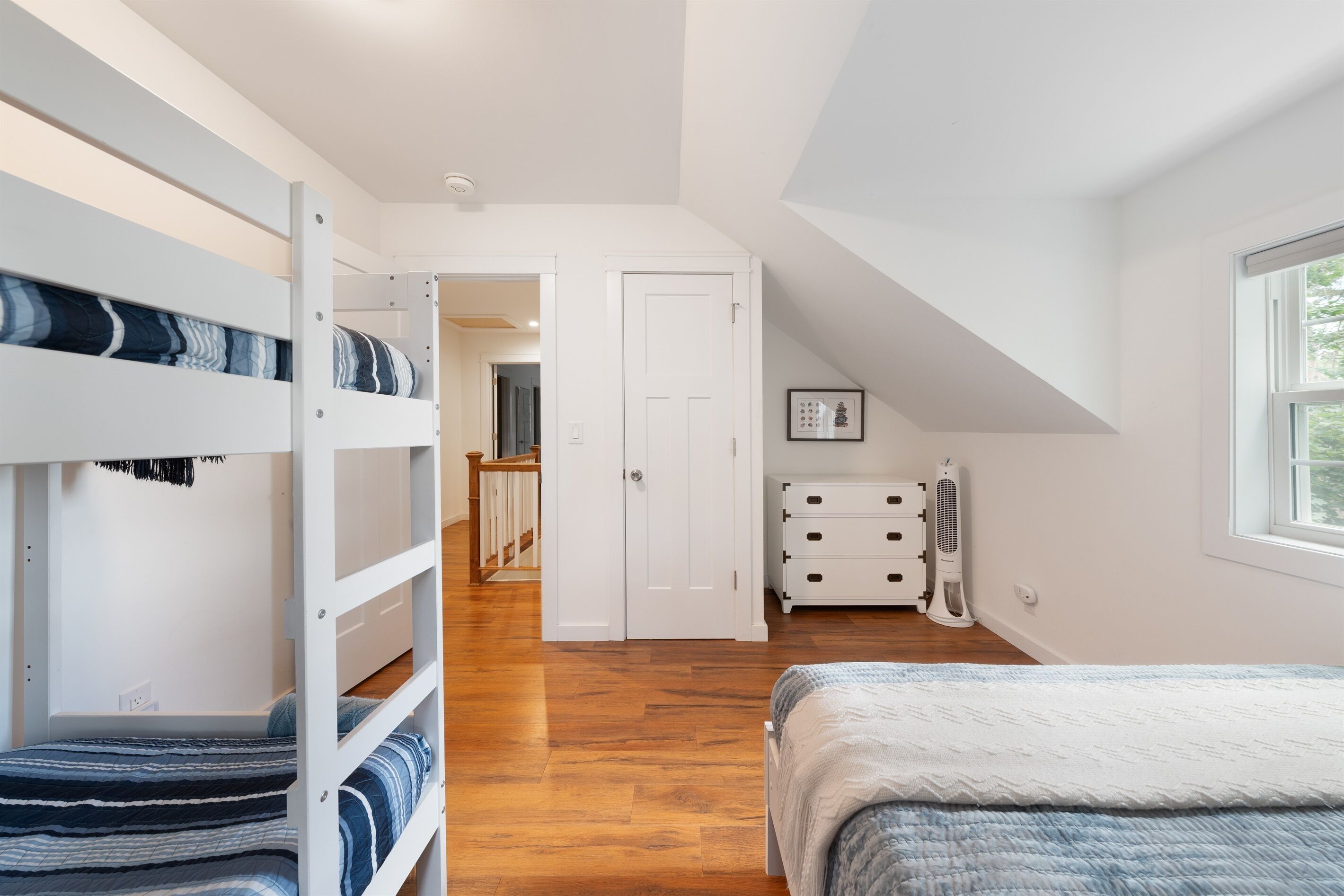 A bedroom with bunk beds, a dresser, a fan, and a window.
