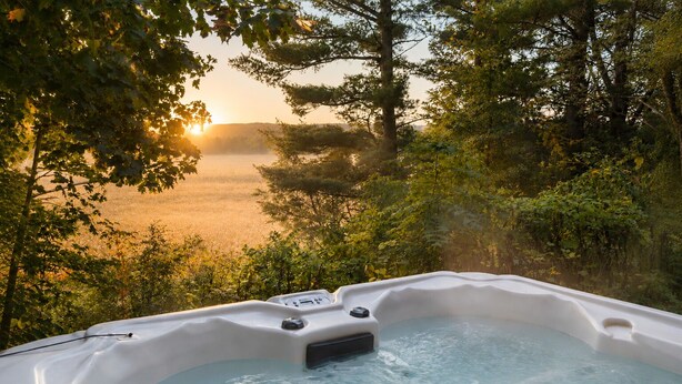 Un jacuzzi rodeado de exuberante vegetación y vistas a un cuerpo de agua al atardecer.