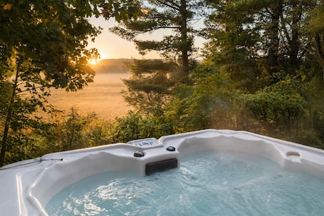 A hot tub surrounded by lush greenery and a view of a body of water during sunset.
