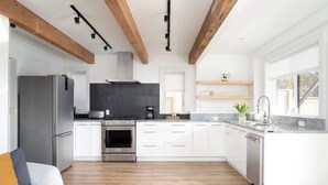 A modern kitchen with white cabinets, stainless steel appliances, and wooden beams on the ceiling. - Romantic modern condo by the lake (Bellevue)