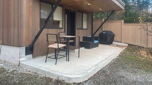 A covered patio area with a table and chairs, a grill, and a wooden deck. - Romantic modern condo by the lake (Bellevue)